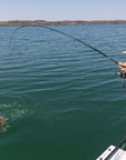 A man hooked a fish and is holding onto his pole, while the fish is thrashing around in the water. 