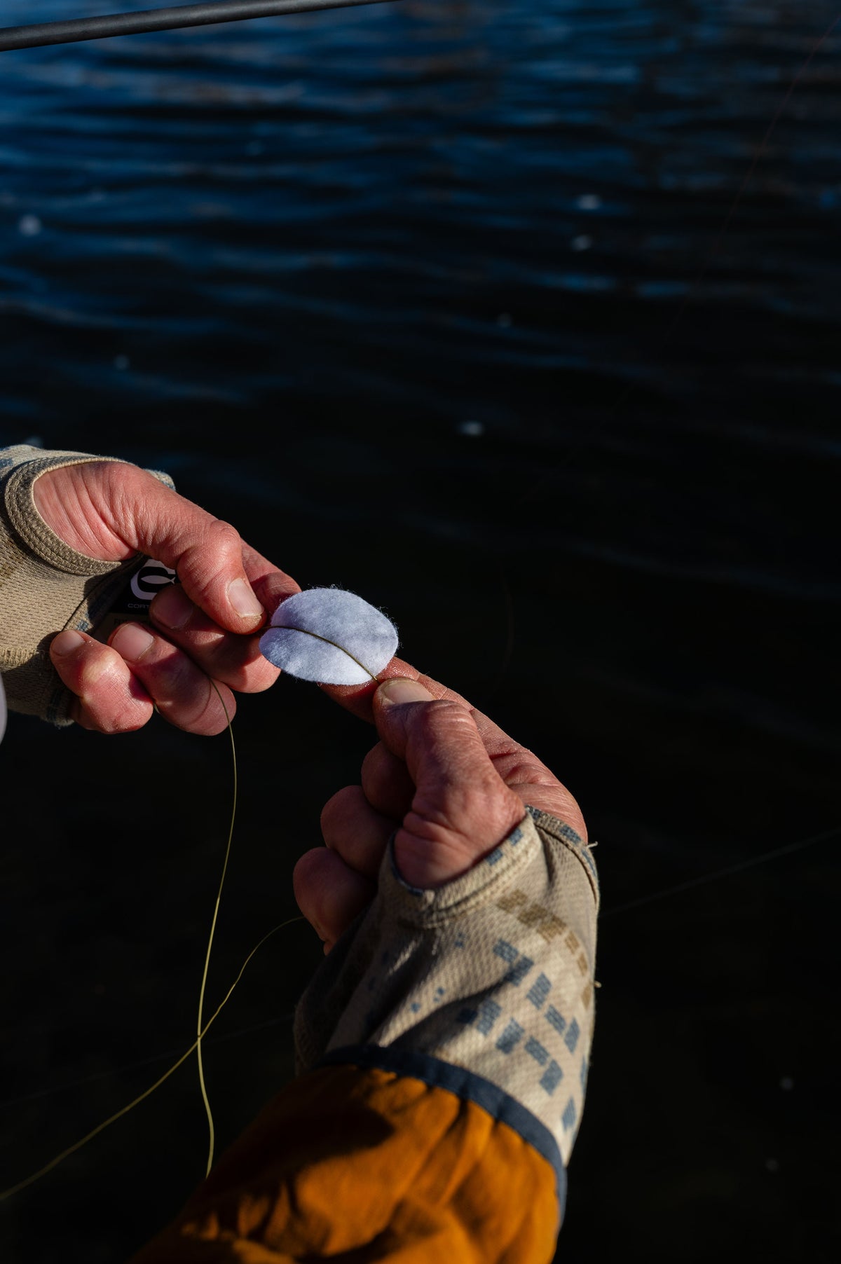 Close-up of hands using a lubricated pad to clean fly line with water in the background