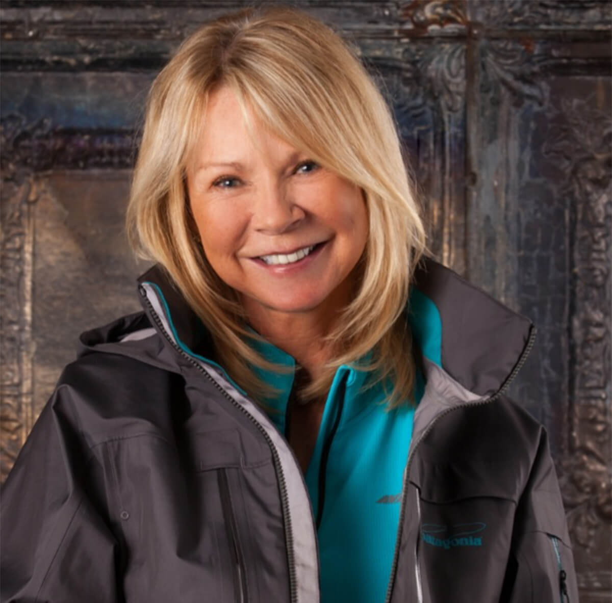 Wanda Taylor is smiling at the camera with a grey jacket on and a light blue shirt underneath 