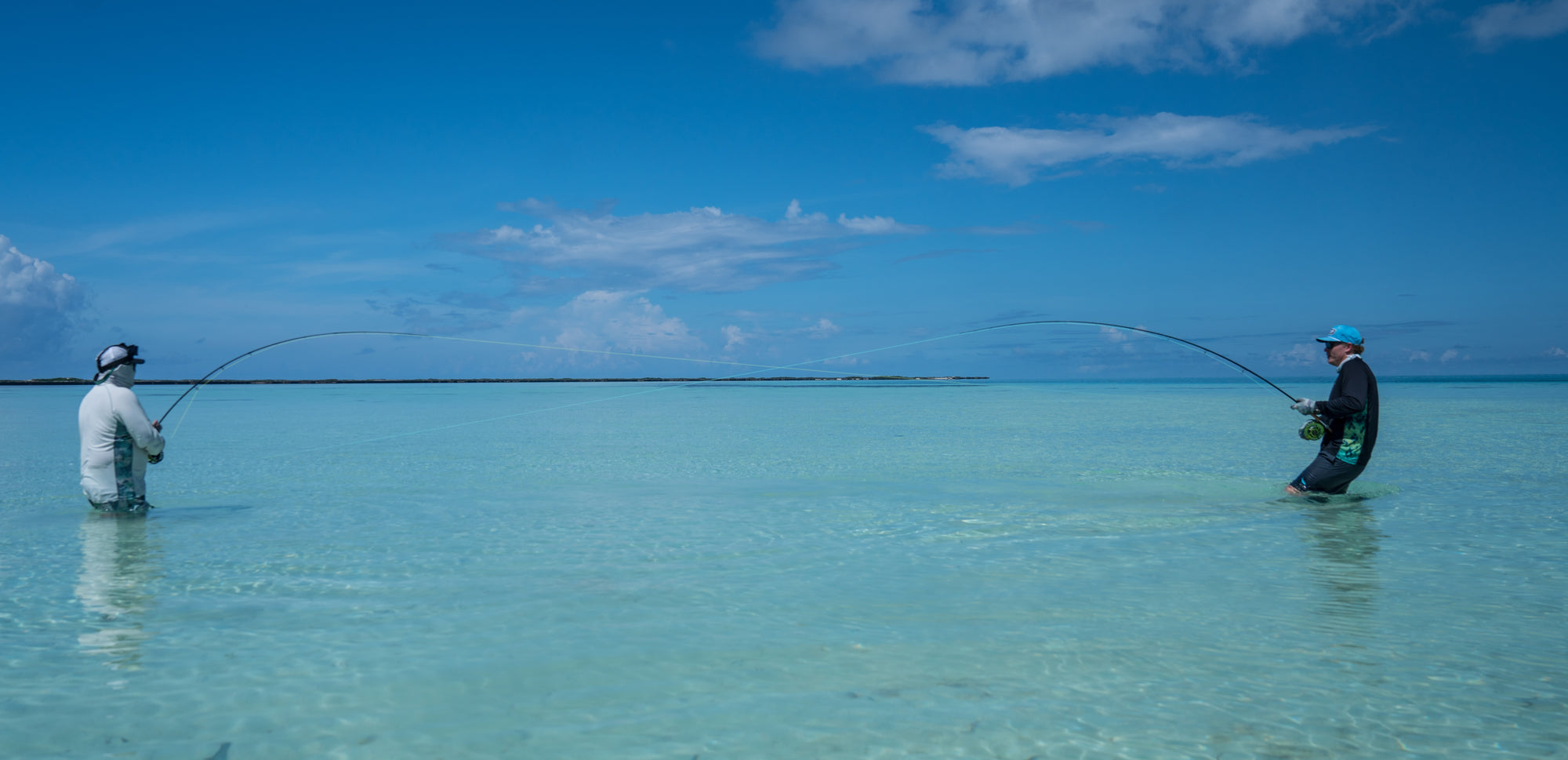 Two people fly fishing in clear blue water with a bright blue sky.